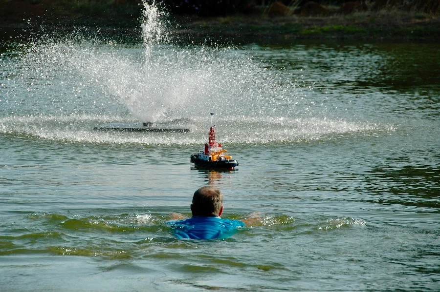 Man swimming in lake toward model tugboat
